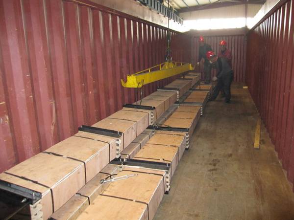 Three workers are loading the polished rod in an open top container.